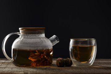transparent teapot and glass with blooming tea on wooden table isolated on black