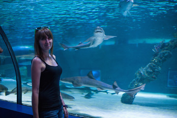Young girl in aquarium tunnel with sharks. Silhouette of a young beautiful girl on the background...