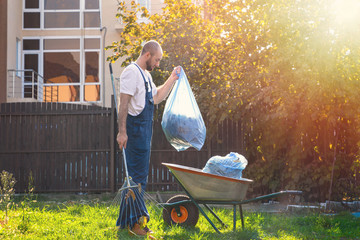 The gardener collects the bags of leaves and puts them in the cart. The sun shines brightly on the...