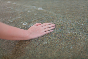 Beautiful female hand in the sand. Girl with a wedding ring. Honeymoon on the sea beach. Ring on the hand against the background of the sea and the beach