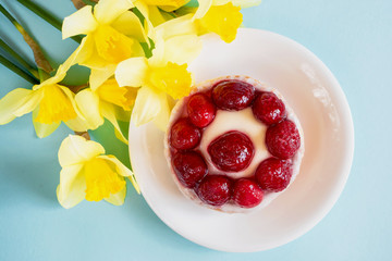 black tea in a white cup on a white saucer on a blue paper background and flowers of yellow daffodils