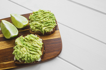 sandwiches with avocado puree and sesame on a wooden board on a light wooden background with free space on the right for blog posts