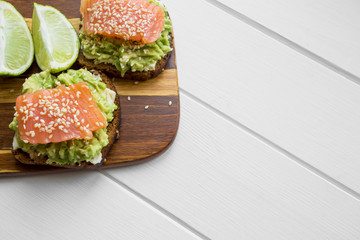sandwiches with mashed avocado and red fish salmon with sesame on a light wooden background with free space for writing on blogs