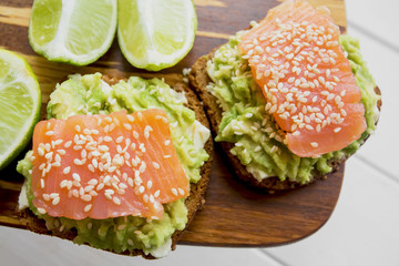 sandwiches with pasta made from avocado and red fish salmon with sesame and lying nearby sliced ​​lime close-up