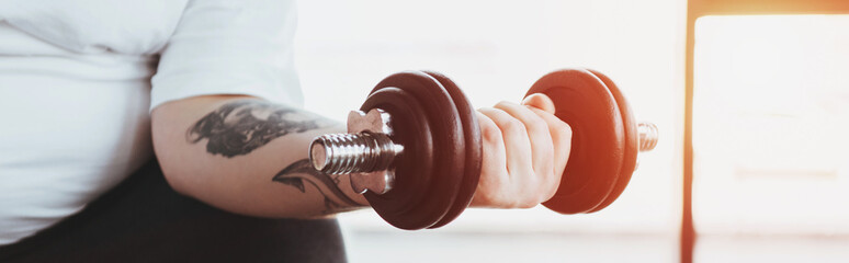panoramic shot of Overweight tattooed man training with dumbbell at gym