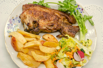 Fried potatoes and large piece of roast pork with cabbage salad, sliced carrots with pieces of radish and a sprig of cilantro on a porcelain plate