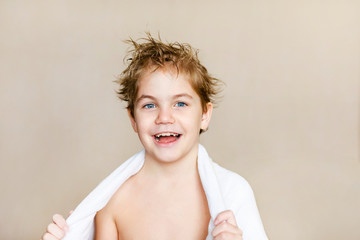 Blode caucasian boy after bath with wet hair and white towel on the shoulders laughing and showing ok hand sign over brown background