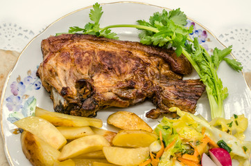 Large piece of roast pork and  fried potatoes with cabbage salad, sliced carrots with pieces of radish and a sprig of cilantro on a porcelain plate