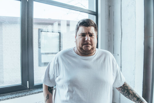 overweight tattooed man in white t-shirt looking at camera at gym