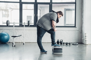 overweight man with towel exercising on step platform at sports center