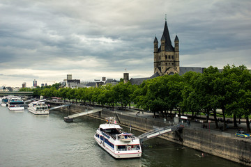 Picturesque view of Cologne central part of city in Germany across the Rhine river. The Great Saint Martin Church on the other side of Rhine. Moored cruise liners and boats on the river Rhine bank.