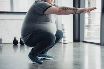 cropped view of overweight tattooed man doing squats at sports center