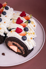 Chocolate roll cake with berries and fresh cream on brown background.