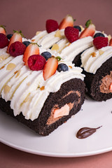 Chocolate roll cake with berries and fresh cream on brown background.