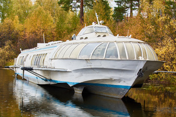 Abandoned big boat for transporting people stands on shore of lake.