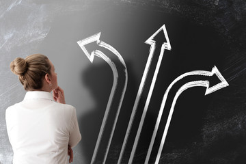 decision making concept with rear view of woman looking at chalkboard with arrows pointing in...