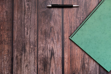 View of an office table with a pen and a notebook on top of it in flat lay top view.