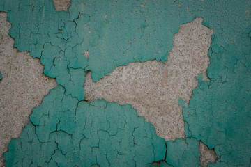 Old grunge weathered crumbled peeling green painted plastered house wall surface detail close up as background.