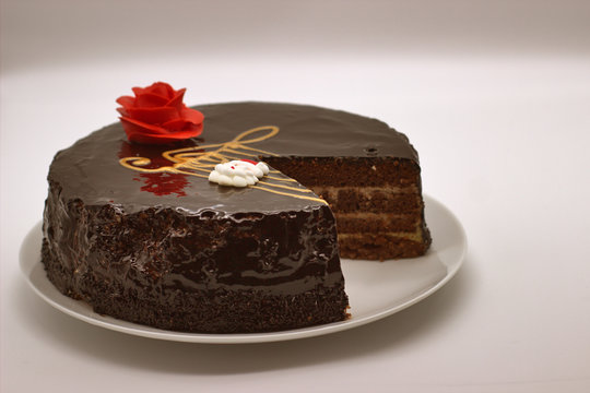 Chocolate cake on a white background. Image from above. The cake is decorated with a red flower of cream and a stylized musical style with a G-Clef