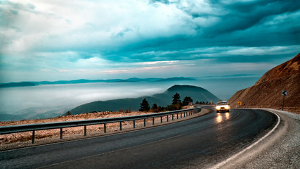 car going by the road between foggy and cloudy mountains