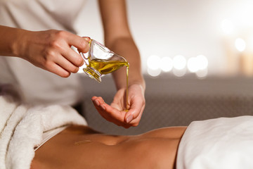 Masseur pouring oil on hand, preparing for massage