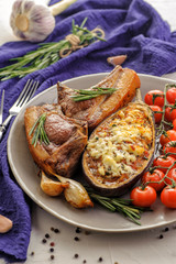 Baked eggplants with roasted meat, tomatoes and cheese. Traditional dish of the Balkan cuisine. A large portion on a plate and a blue napkin on a light background. Ketogenic food. Vertical view.