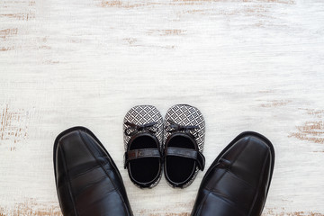 Father's business black shoes and daughter's baby black shoes on rustic white wood background. Concept of family, single parent and father's day. Flat lay top view with copy space. - Powered by Adobe