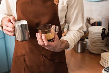 Partial view of barista holding cup of coffee and milk jug