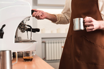Cropped view of barista in brown apron preparing coffee
