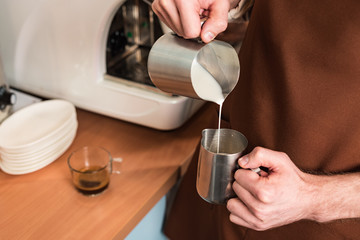 Fototapeta na wymiar Cropped view of barista in brown apron pouring milk in steel jug