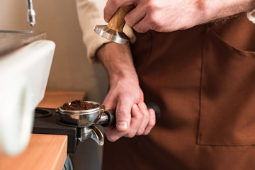 Partial view of barista holding portafilter with ground coffee and tamper