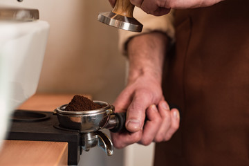 Cropped view of barista in brown apron preparing coffee