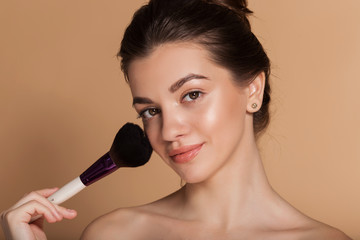 Closeup portrait of beautiful happy young girl with perfect skin is holding makeup brush in hand....