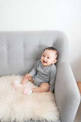 Closeup portrait of cute adorable smiling laughing, baby girl with black eyes sitting on sofa looking away from camera, natural window light, lifestyle