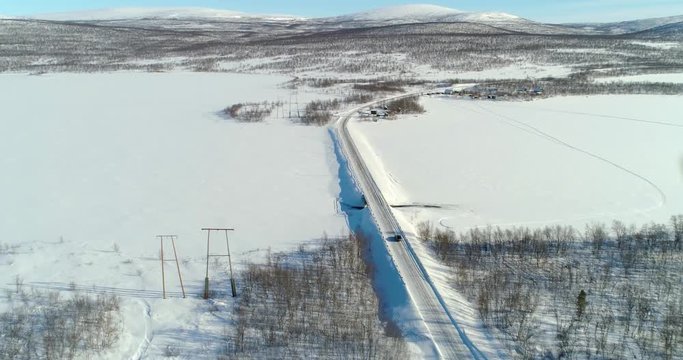 Aerial, drone shot, of a car on route e8, between frozen polar lake and boreal wilderness, in Kasivarren eramaa, Enontekio, Lapland, Finland