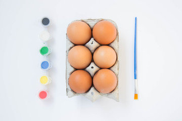 Easter brown chicken eggs in carton container, with paints, colorful palette, paint equipment on white background