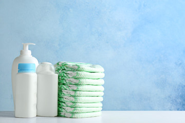 Stack of diapers and toiletries on table against color background, space for text. Baby accessories