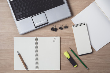 Workspace with diary or notebook and laptop, pen, pencil, hightlight pen, metal clip on wooden background