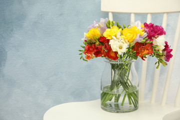 Beautiful spring freesia flowers in vase on chair. Space for text