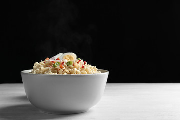 Bowl of hot noodles with egg and vegetables on table against black background. Space for text
