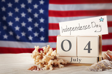 Composition with wooden calendar and card on sand against USA flag, space for text. Happy Independence Day