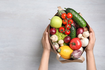 Woman holding paper bag with fresh vegetables on light background, top view. Space for text