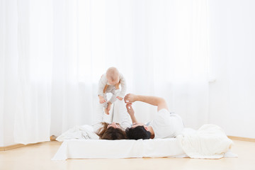 Portrait of young parents playing with little one-year old baby boy on bed indoors. Smiling baby...