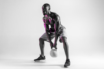 Young african-american bodybuilder training over grey background