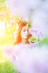 Young brunette stands in the lilac bushes. Bright sunny day.