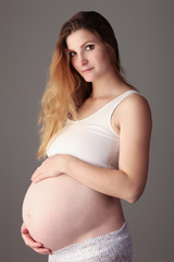 Pregnant woman caressing her belly over a gray background