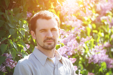 A man stands in the lilac bushes on a bright sunny day.