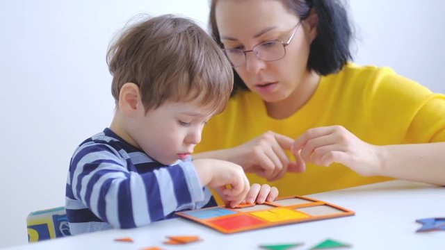 little asian boy collects puzzles with mom sitting at the desk. A cute child collects a picture from large multi-colored details. Playing with a puzzle. slow motion. Teacher playing with boy