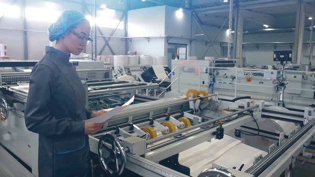 Asian woman worker checking how flexographic machine for multicolor printing on paper.