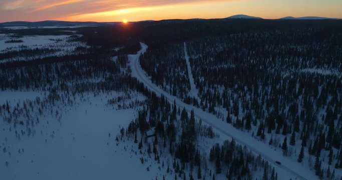 drone shot, following a vehicle, on a frozen route, between finnish woods and polar wilderness, in Pallas-yllastunturi national park, at the arctic circle, at sunset, on a sunny, winter evening dus